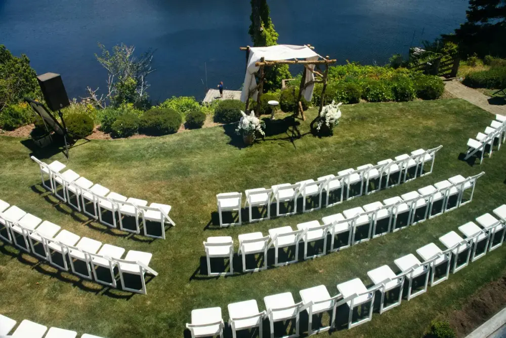 Curved rows of white chairs set out for an outdoor wedding ceremony beside a lake