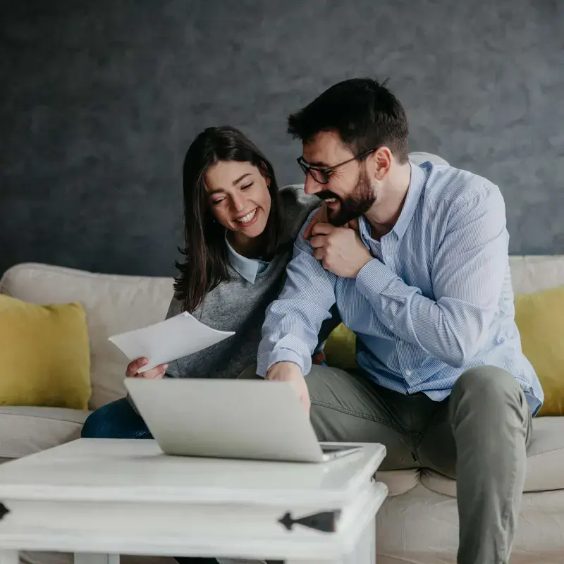 A couple on a sofa going through papers and a laptop together, planning their payments