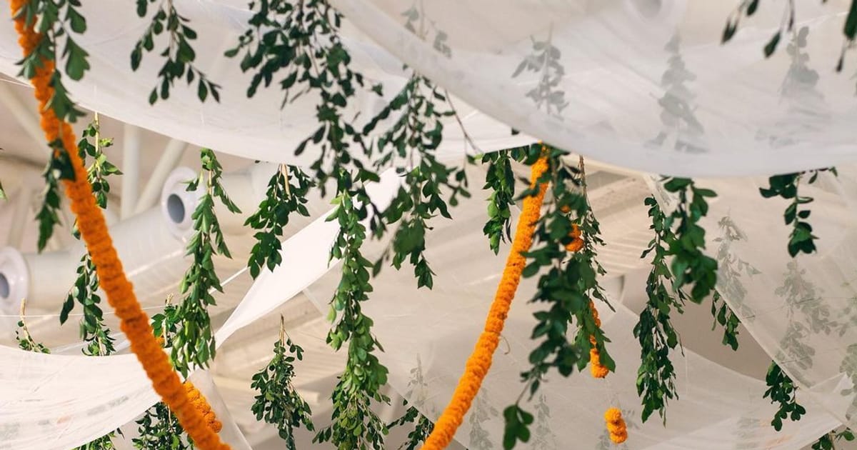 Orange marigold garlands and green leaves hanging from soft white drapes at a wedding venue