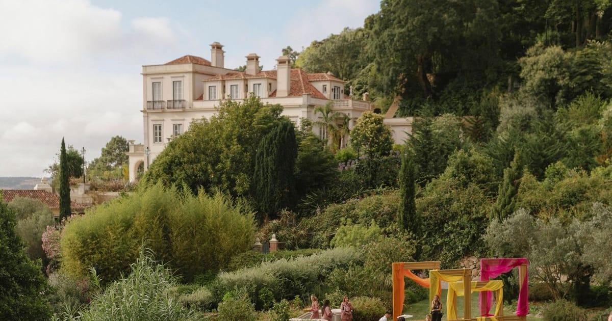 A villa surrounded by gardens, with guests gathering at a wedding celebration on the lawn